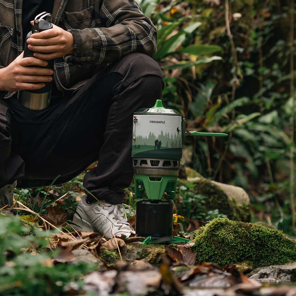 Person in a forest setting with a camping stove and thermos#color_green
