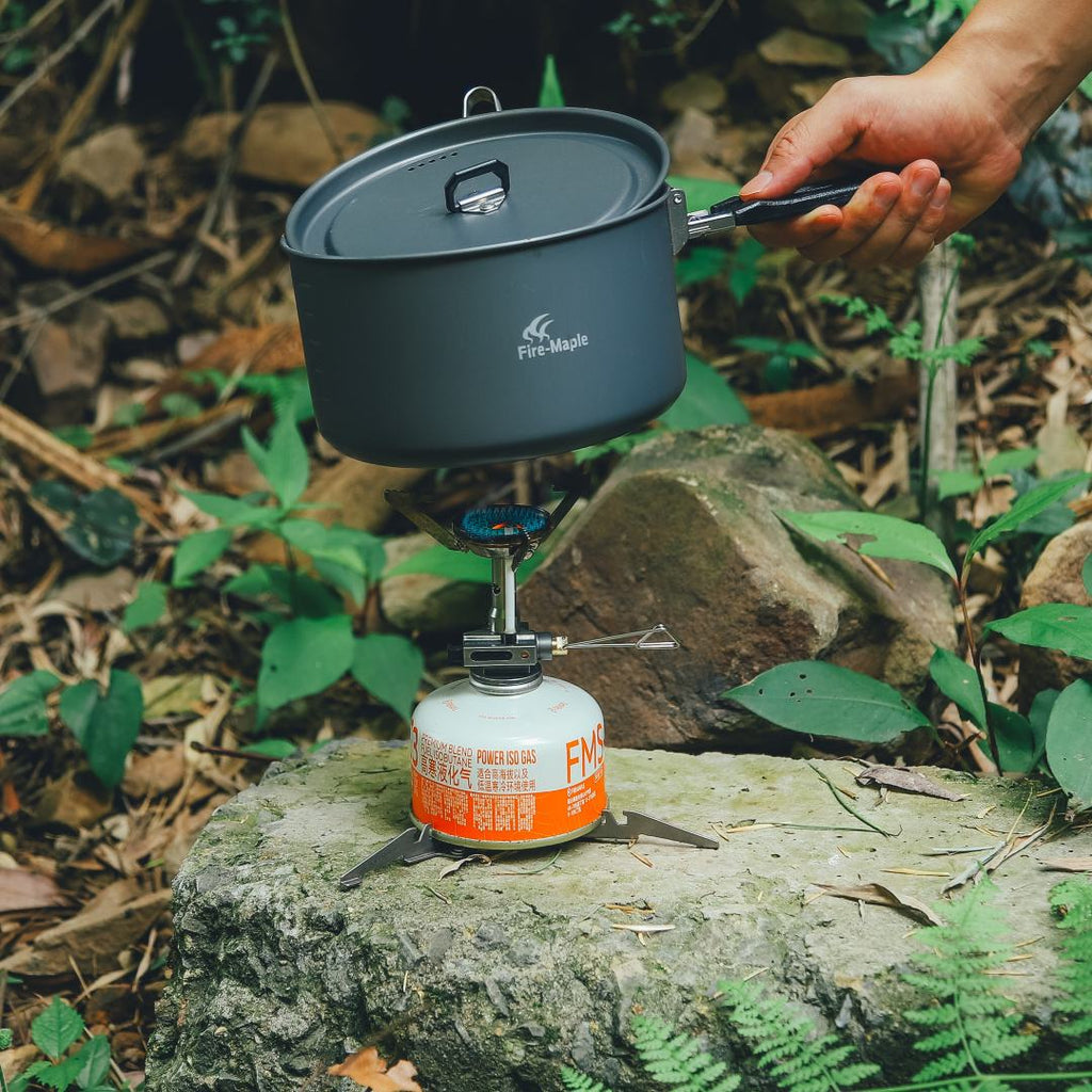 Person holding a camping pot over a portable stove in a natural setting #color_pressure_regulated